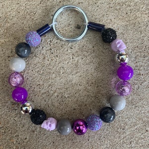 May include: A purple, gray, and black beaded keychain with a silver ring and skull charms.