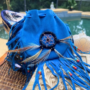May include: A blue suede pouch with a dreamcatcher design and fringe. The pouch is decorated with feathers and beads.