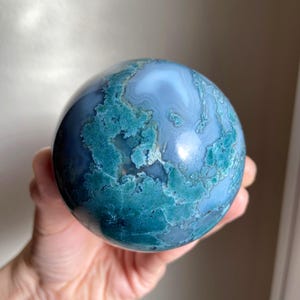 Pu&ograve; includere: Una sfera lucidata in agata muschiata, che mostra una miscela di tonalit&agrave; blu e verde acqua. La superficie della gemma presenta motivi intricati, creando un oggetto decorativo unico. Questa sfera di pietra naturale &egrave; una bella aggiunta a qualsiasi collezione.