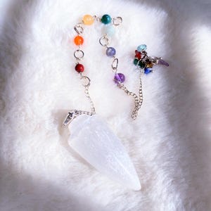 May include: A white, pointed, translucent crystal pendulum attached to a silver-toned metal chain. The chain features a series of small, round, multi-colored beads in shades of red, orange, yellow, green, light blue, dark blue, and purple.