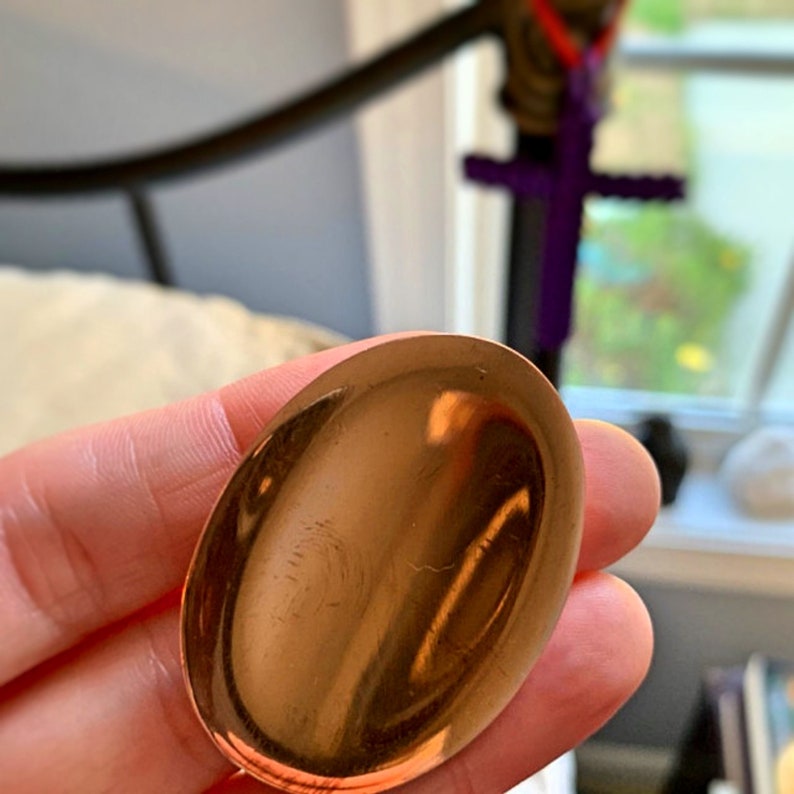 May include: A smooth, oval-shaped, copper-colored stone with a shiny finish.