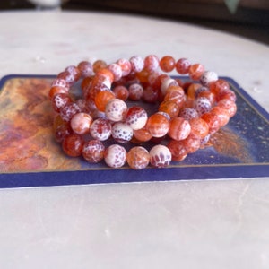 May include: A stack of three bracelets made of orange and white agate beads. The beads have a speckled pattern.