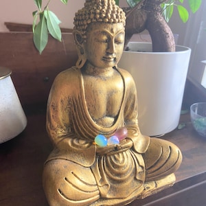 May include: A gold-painted statue of Buddha sitting in meditation with three iridescent gemstones in his lap.