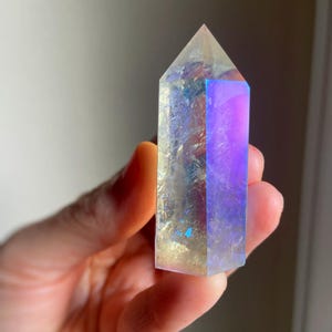 Puede incluir: Una punta de cristal hexagonal con acabado pulido, que muestra una apariencia transl&uacute;cida con fracturas internas y un revestimiento iridiscente vibrante que refleja tonos azules, p&uacute;rpuras y dorados en su superficie facetada.