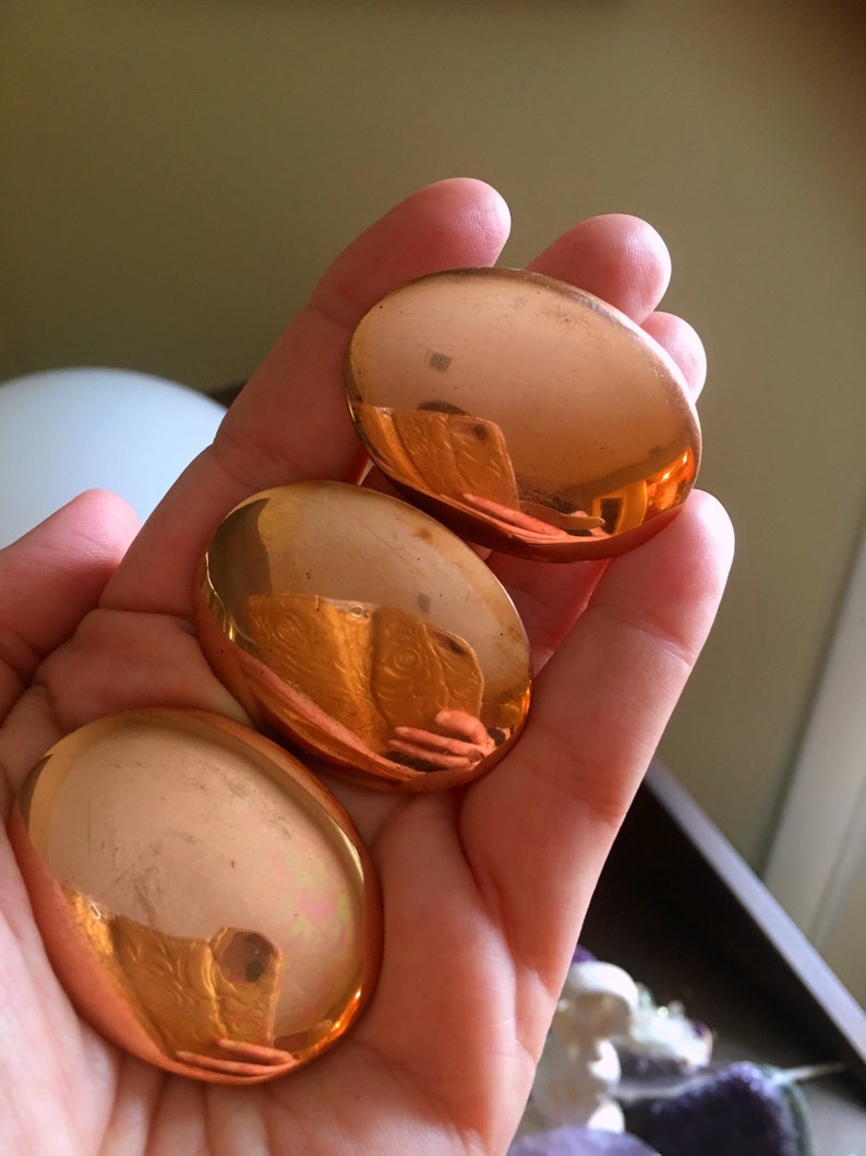 May include: Three smooth, oval-shaped copper stones, each with a reflective, metallic finish. The stones are arranged in a stack, with the largest stone at the bottom and the smallest stone at the top.