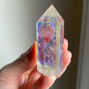 Puede incluir: Una punta de cristal hexagonal con acabado pulido, que presenta una base transl&uacute;cida amarilla y clara con un revestimiento met&aacute;lico iridiscente tipo arco&iacute;ris que refleja tonos azules, p&uacute;rpuras y dorados sobre su superficie facetada.