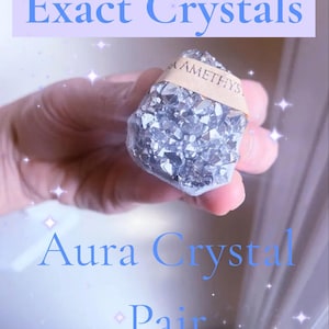May include: A close-up of a cluster of shimmering, silver crystals labeled "AMETHYST" with a light brown band. The image has text that reads "Exact Crystals" and "Aura Crystal Pair" in blue.