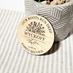 May include: A round wooden sign with the text "Our Roots Run Deep" and a tree design. The sign also includes the name "Wyckoff" and the date "6.28.25". The text "Family Reunion" is at the bottom of the sign.