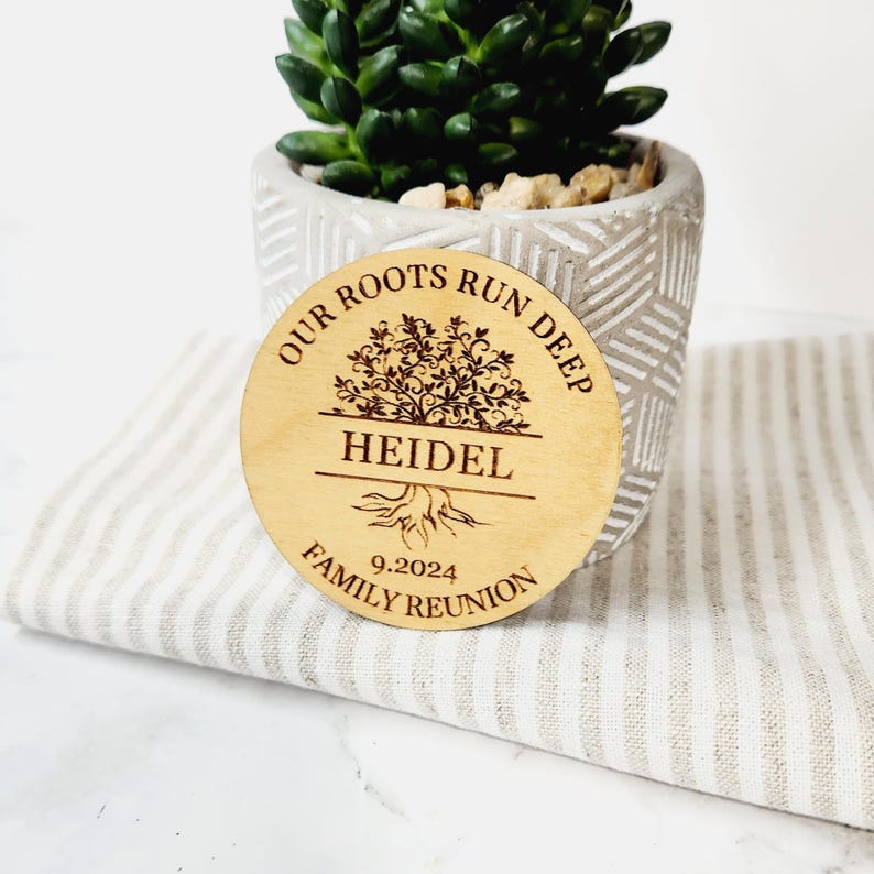 May include: A round wooden sign with the text "Our Roots Run Deep" and a stylized tree design. The name "Heidel" is engraved below the tree, and the date "9.2024" and the text "Family Reunion" are engraved below the name.