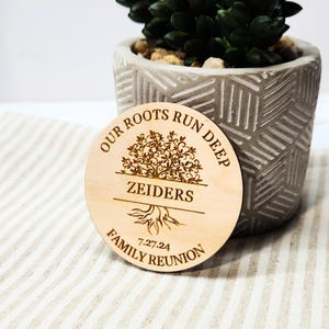 May include: A wooden round sign with the text "Our Roots Run Deep" and a stylized tree with roots. The text "Zeiders Family Reunion 7-27-24" is also on the sign.