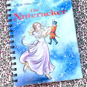 May include: A spiral-bound Little Golden Book titled The Nutcracker, featuring a watercolor illustration of a person in a light purple dress dancing with a nutcracker toy against a blue background with white sparkles and the number 460-15.