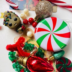 May include: A collection of Christmas-themed items including a small brown tree-like figure with colorful lights, a red and white candy cane, a gold glitter ornament, a round peppermint-patterned tin, a red lightbulb ornament, and green beads.