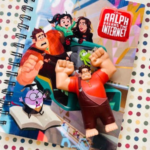 May include: A spiral-bound "Little Golden Book" notebook featuring characters from "Ralph Breaks the Internet." The cover displays Ralph, Vanellope, and other characters. A Ralph figurine is posed in front of the notebook.
