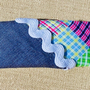 Peut inclure: Un rectangle de tissu denim bleu avec un bord festonné blanc. L'autre côté du rectangle est fait d'un patchwork de tissus à carreaux colorés.