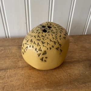 May include: A yellow ceramic vase with a geometric pattern in black. The vase is shaped like a rounded rock.