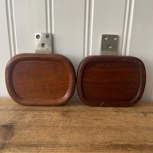 May include: Two wooden serving trays with rounded corners and a dark brown finish. Each tray has a rectangular shape and is attached to a metal bracket with three holes. The trays are displayed on a wooden surface.