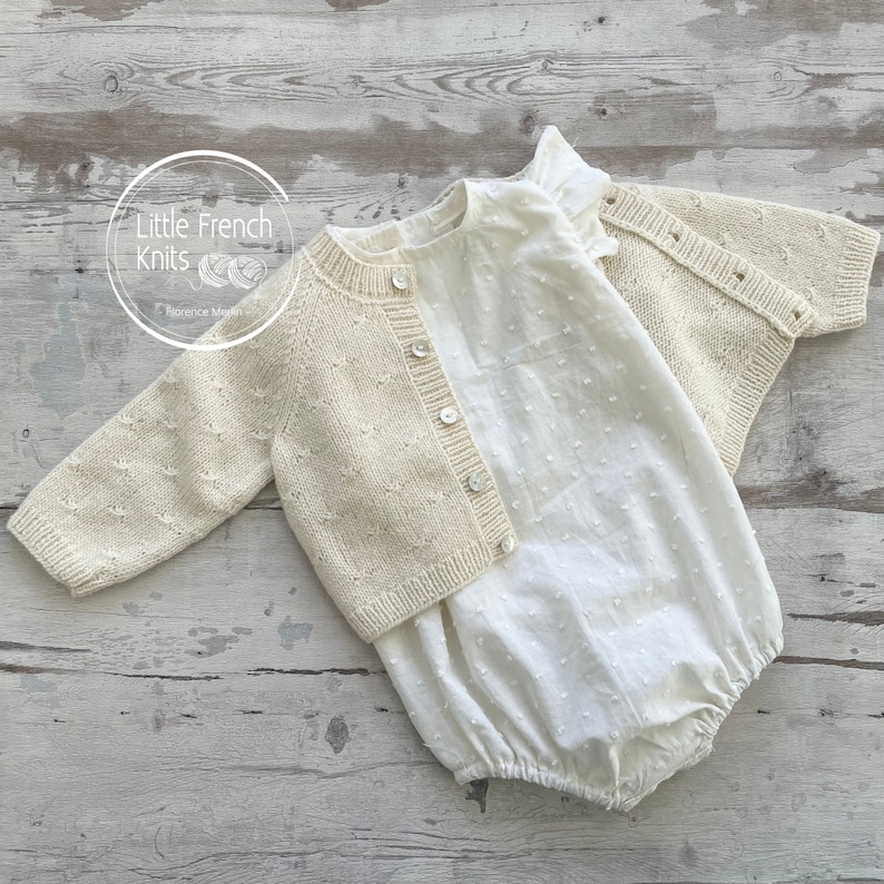 Puede incluir: Un c&aacute;rdigan de punto color crema con cierre de botones y un body de algod&oacute;n blanco con estampado de lunares. El conjunto est&aacute; colocado sobre una superficie de madera clara. El texto "Little French Knits" es visible en la imagen.