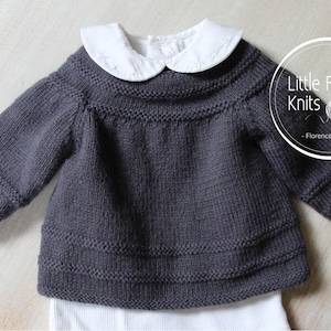 Puede incluir: Un jersey de punto gris oscuro para bebé con un cuello blanco Peter Pan. El jersey tiene una textura acanalada y una forma ligeramente acampanada. El texto "Little French Knits - Florence Merlin" es visible en la esquina superior derecha de la imagen.