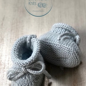 May include: A pair of gray knitted baby booties with a bow tie detail. The booties are on a wooden surface.  Little French Knits - Florence Merlin -