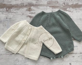 May include: Two knitted baby garments, one a cream cardigan and the other a sage green romper. Both garments feature a delicate cable knit pattern.