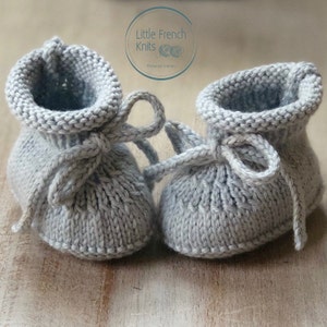 May include: A pair of gray knitted baby booties with a tied bow on each. The booties are made with a simple stitch pattern and have a soft, cozy look.