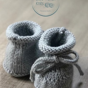 May include: A pair of gray knitted baby booties with a bow tie. The booties are made with a simple stitch pattern and have a soft, comfortable feel.