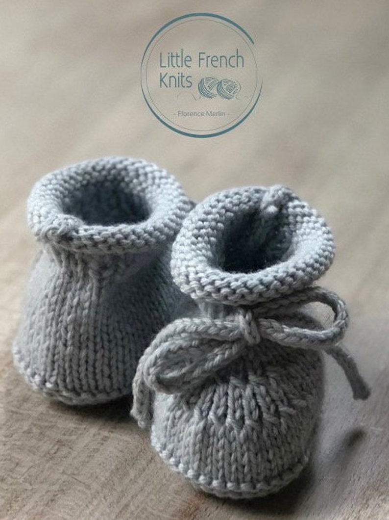 May include: A pair of gray knitted baby booties with a bow tie. The booties are made with a simple stitch pattern and have a soft, comfortable feel.