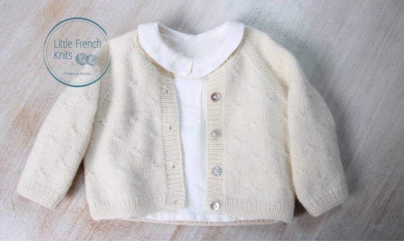 Puede incluir: Un c&aacute;rdigan de punto color crema con un delicado patr&oacute;n calado y botones nacarados. El c&aacute;rdigan se muestra con una camisa blanca de cuello debajo.