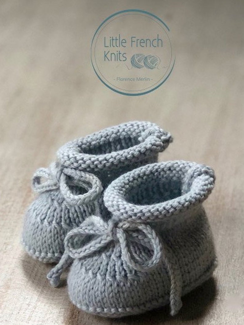 May include: A pair of gray knitted baby booties with a bow on each. The booties are made with a simple stitch pattern and have a soft, cozy look.