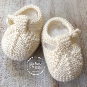 Peut inclure: Une paire de chaussons bébé en tricot blanc avec une bride et un bouton. Les chaussons sont faits avec un motif de point délicat et ont une doublure douce et moelleuse.