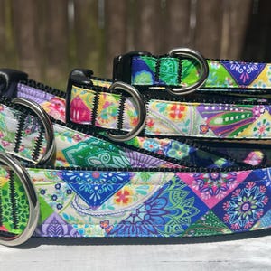 May include: A stack of three pet collars featuring a vibrant, multi-coloured patchwork pattern with intricate mandala and floral designs in shades of blue, green, pink, and yellow. Each collar includes a black plastic buckle and a silver metal D-ring.