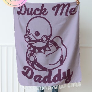 Może przedstawiać: Fioletowy koc szydełkowy z kreskówkową kaczką w obroży i napisem "Duck Me Daddy".