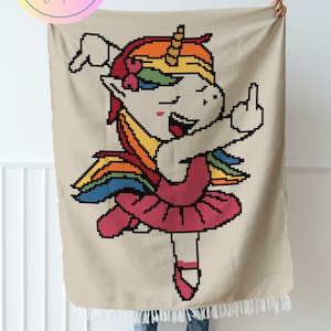 May include: A crochet blanket featuring a pixelated unicorn wearing a pink tutu and giving the middle finger. The unicorn has a rainbow mane and a yellow horn. The blanket is beige with a white fringe.