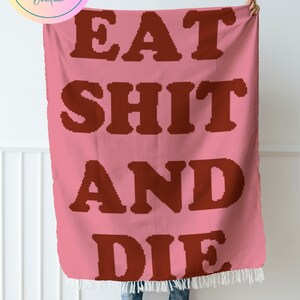 Puede incluir: Una manta de crochet rosa con la frase "EAT SHIT AND DIE" en letras rojas.
