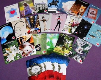 Puede incluir: Una baraja de cartas de juego francesas con ilustraciones coloridas en cada carta. Las cartas están dispuestas en forma de abanico sobre una superficie morada. Las cartas presentan imágenes de una casa, un jinete, nubes, un zorro, un libro, un látigo, un hombre, una mujer, una luna, lirios, un ratón, un perro, un trébol, un parque y peces.
