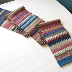 Può includere: Due runner da tavolo tessuti con un motivo geometrico in tonalità di marrone, blu, rosa e bianco.