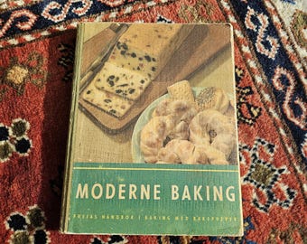 Könnte beinhalten: Ein altes Kochbuch mit grünem Einband und dem Titel "Moderne Baking". Auf dem Einband ist ein Bild von einem Früchtekuchen und Gebäck zu sehen.