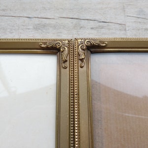 Può includere: Una cornice per foto dorata con dettagli decorativi. La cornice è divisa in due sezioni, ciascuna con un pannello di vetro trasparente.
