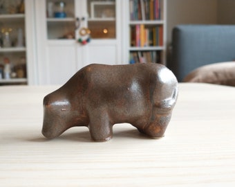 May include: A brown ceramic sculpture of a bull, with a textured surface and a slightly rounded shape.