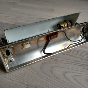 May include: A silver metal wall light fixture with a white interior. The fixture has a light bulb socket and wires visible. The fixture has a label that reads "UL Listed".
