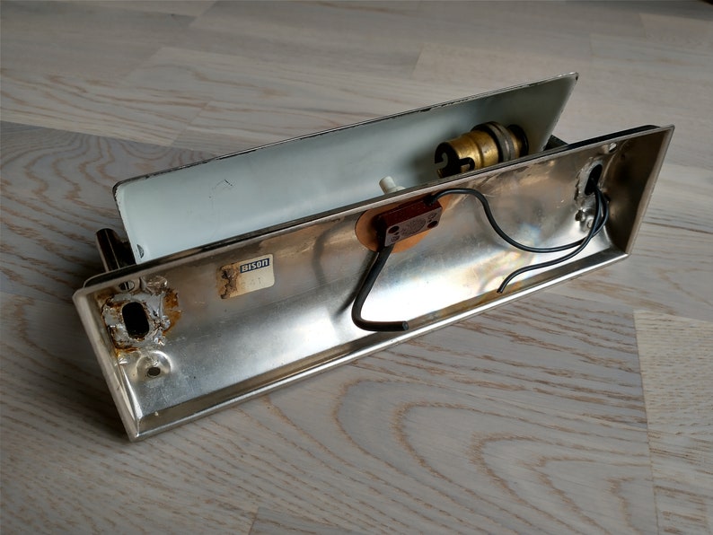 May include: A silver metal wall light fixture with a white interior. The fixture has a light bulb socket and wires visible. The fixture has a label that reads "UL Listed".