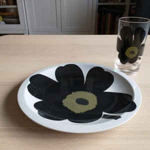 May include: A white ceramic plate with a black and green flower design. A clear glass with a black and green flower design is next to the plate.