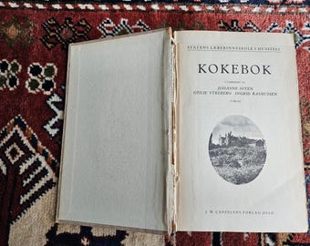 Könnte beinhalten: Ein altes Kochbuch mit dem Titel "KOKEBOK" von Johanne Sveen, Otilie Ytreberg und Ingrid Rasmussen. Der Umschlag zeigt ein Schwarzweißfoto eines Gebäudes mit einem Garten.