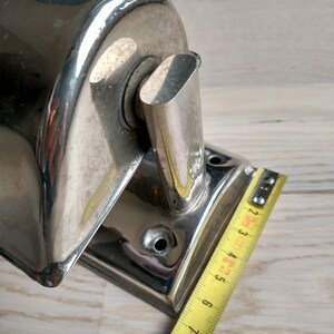 May include: Chrome-plated wall-mounted bathroom tissue holder with a rounded rectangular base and a curved top. The holder is measured with a yellow tape measure.