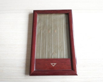 May include: A rectangular, wooden picture frame with a dark reddish-brown finish. The frame has a glass front and a decorative, patterned backing. A small, silver-colored triangle design is at the bottom.