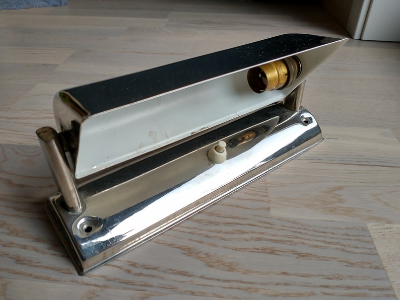 May include: A chrome-plated wall light fixture with a white interior and a light bulb socket. The fixture has a switch on the side and a mounting bracket on the back.