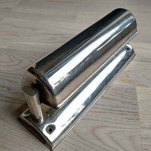 May include: A silver-toned wall-mounted light fixture with a cylindrical shade and a rectangular base.