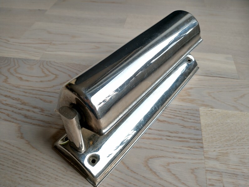 May include: A silver-toned wall-mounted light fixture with a cylindrical shade and a rectangular base.