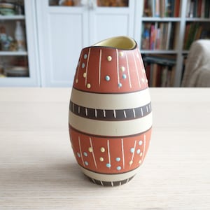 May include: A brown and white ceramic vase with a geometric pattern and colorful dots. The vase is shaped like an egg and has a narrow opening at the top.