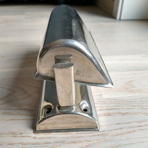 May include: A silver-toned metal doorstop shaped like a boat with a rounded top and a flat base. The doorstop has a small handle on the side and the text "8150" is engraved on the side.